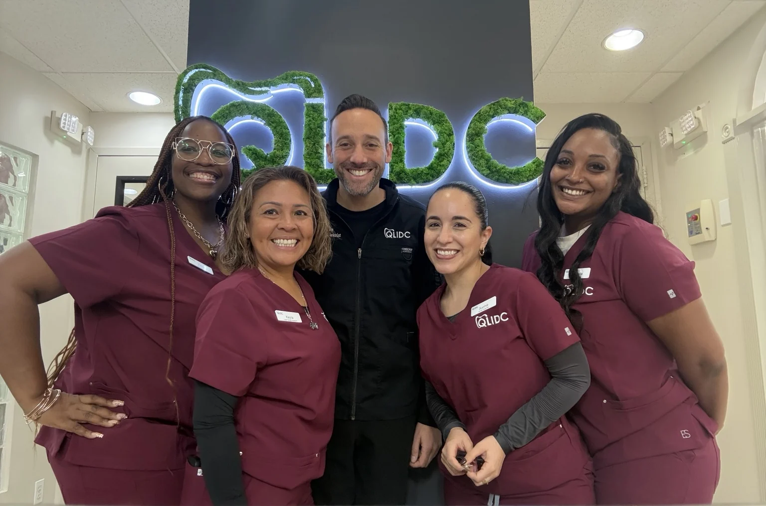 Dr. Ben Schwartz and the QLIDC team in burgundy scrubs beside the office logo